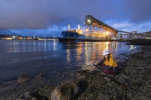 a female with hard hat and yellow jacket with a shore background