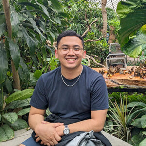 Eman Dapat sitting surrounded by green plants and smiling